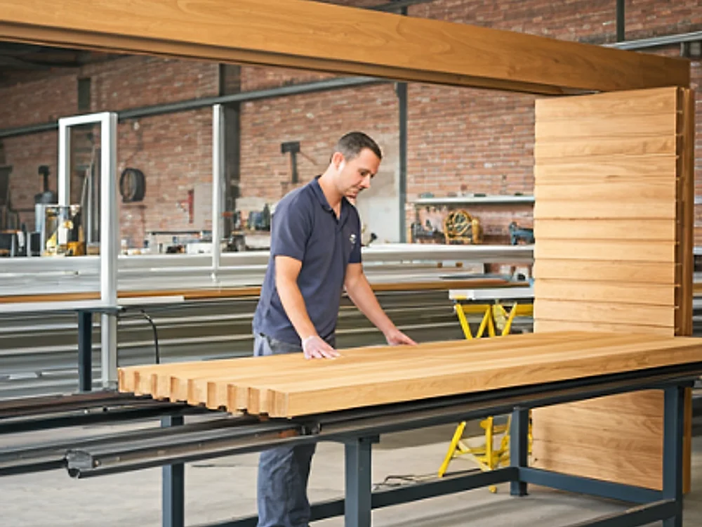 A craftsman building a slatted timber cover at a workbench in the workshop