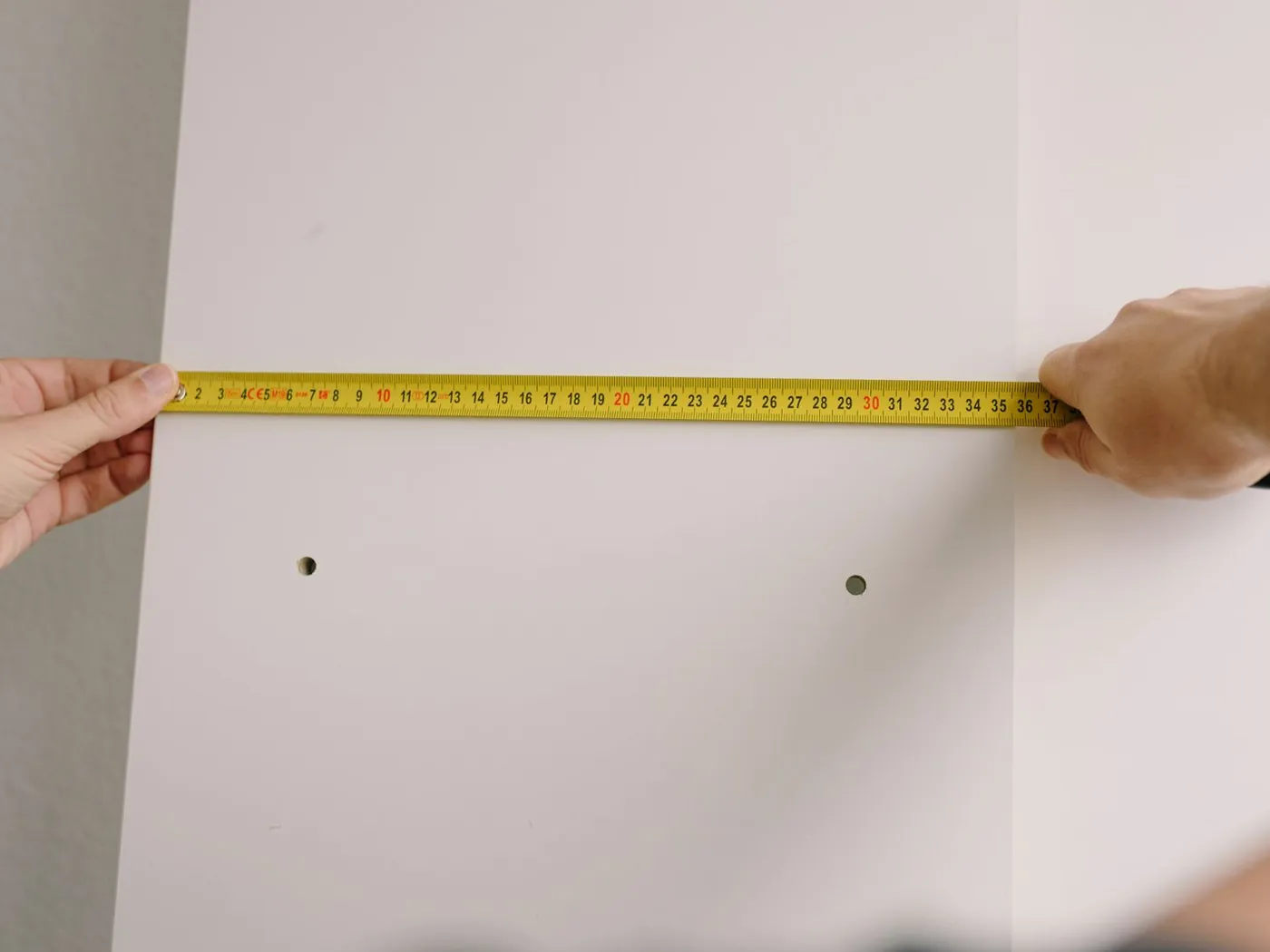 Hands measuring a wall with a yellow tape measure before a cover is made